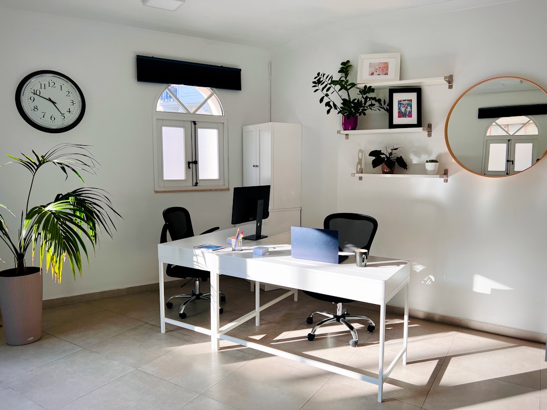 Minimal workspace at FlippingBook with a desk by the window, soft natural light, a wall mirror, and a large indoor plant creating a calm atmosphere.